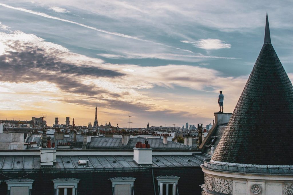 A mesmerizing view of Paris rooftops and the Eiffel Tower at sunset, with a person standing atop a building.